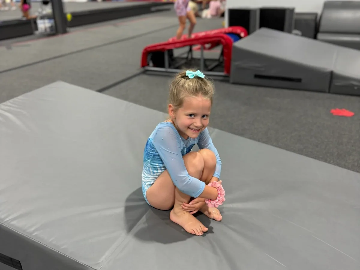 Smiling preschool girl sitting on a tumbling mat at Genesis Athletix