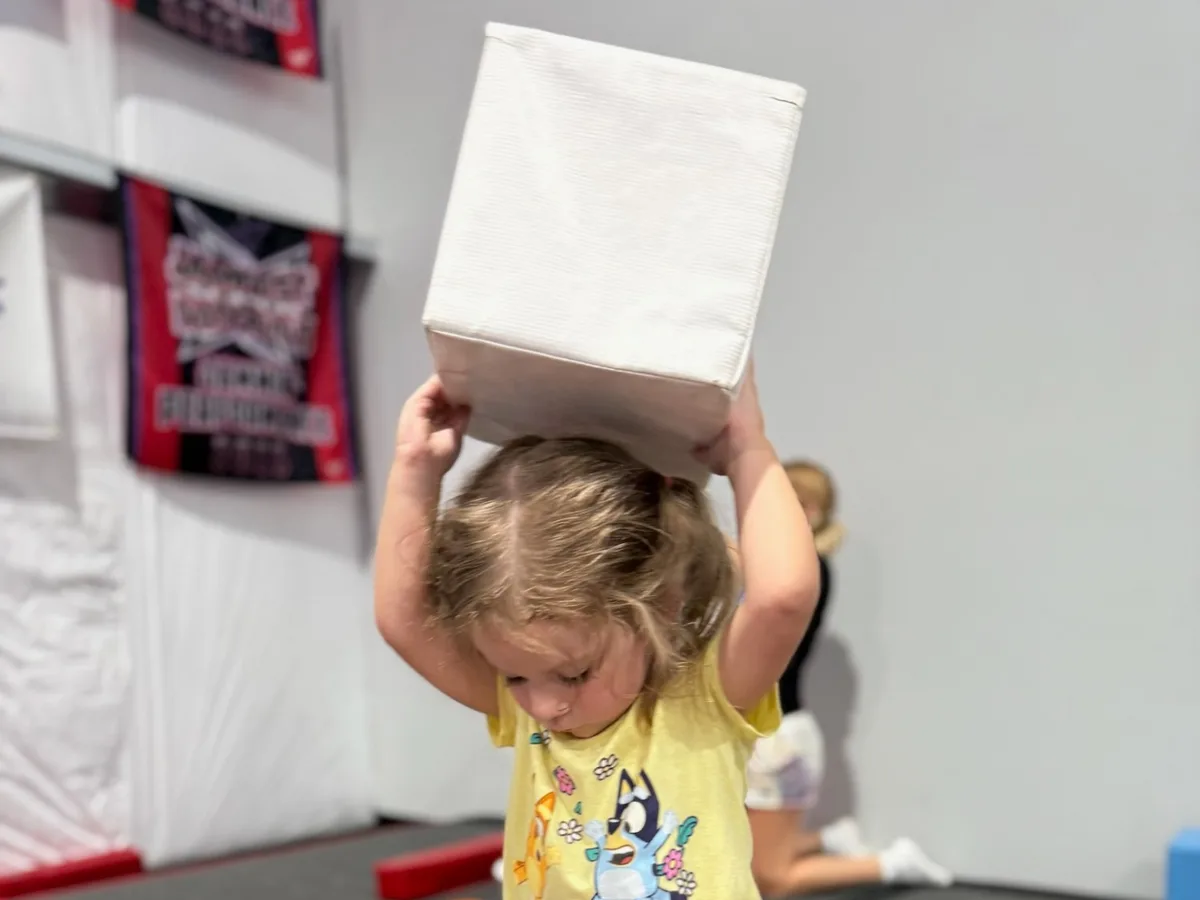 Toddler carrying a soft block during a parent assisted tumbling class at Genesis Athletix